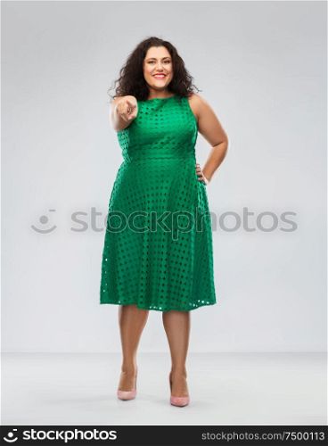 people and portrait concept - happy woman in green dress pointing finger to camera over grey background. woman in green dress pointing finger to camera