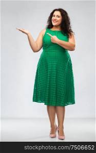 people and portrait concept - happy woman in green dress pointing fingers at something over grey background. happy woman in green pointing fingers at something