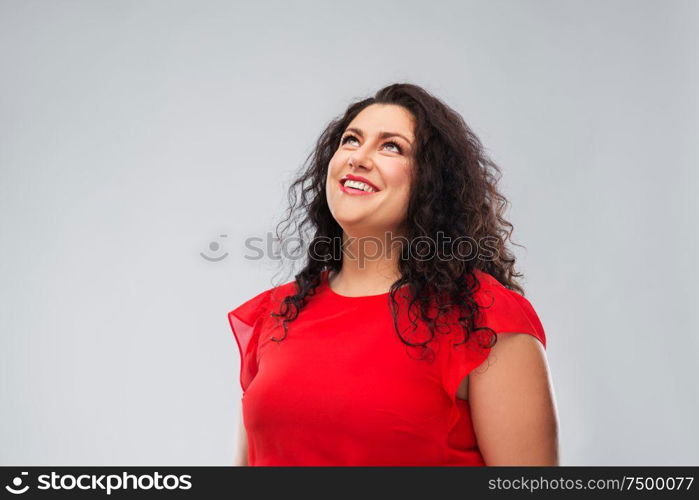 people and portrait concept - happy woman in red dress looking up over grey background. happy smiling woman in red dress looking up