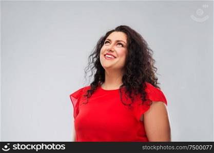 people and portrait concept - happy woman in red dress looking up over grey background. happy smiling woman in red dress looking up