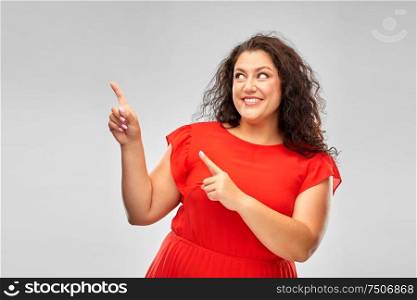 people and portrait concept - happy woman in red dress pointing fingers at something over grey background. happy woman in red pointing fingers at something