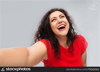 people and portrait concept - happy woman in red dress taking selfie over grey background. happy woman in red dress taking selfie