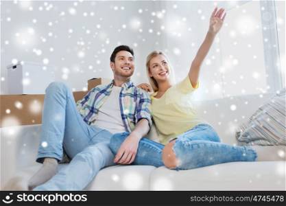people and real estate concept - smiling couple with boxes moving to new home, sitting on sofa and dreaming over snow