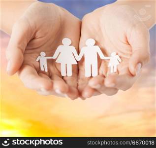people and relations concept - close up of female hands with paper family pictogram over evening sky background. female hands with paper family pictogram. female hands with paper family pictogram