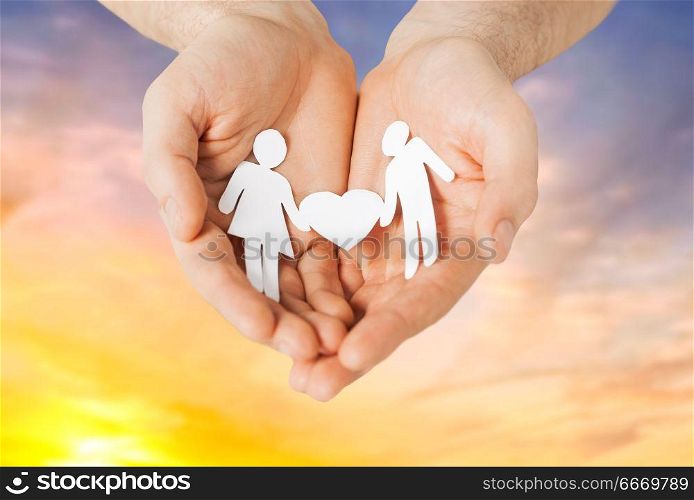 people and relations concept - close up of male hands with paper couple pictogram over evening sky background. male hands with paper couple pictogram. male hands with paper couple pictogram