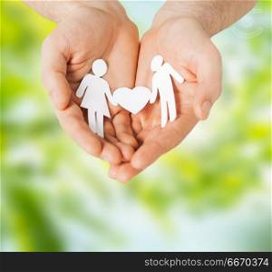 people and relations concept - close up of male hands with paper couple pictogram over green natural background. male hands with paper couple pictogram. male hands with paper couple pictogram