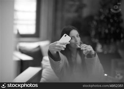 people, and relaxation concept beautiful young woman in bath robe drinking champagne and doing selfy at spa over holidays lights background