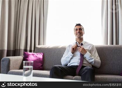 people and rest concept - happy smiling businessman taking off his tie at hotel room. happy businessman taking off his tie at hotel room