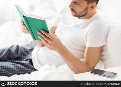 people and rest concept - man reading book in bed at home. man reading book in bed at home