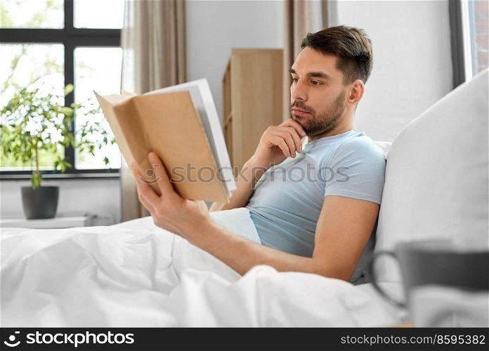 people and rest concept - man reading book in bed at home. man reading book in bed at home