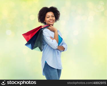 people and sale concept - smiling afro american woman with shopping bags over summer green lights background. smiling afro american woman with shopping bags