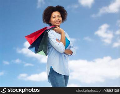 people and sale concept - smiling afro american woman with shopping bags over blue sky and clouds background. smiling afro american woman with shopping bags