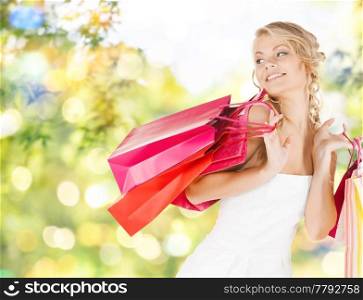 people and sale concept - young smiling woman with shopping bags over green background and lights. young woman with shopping bags over lights