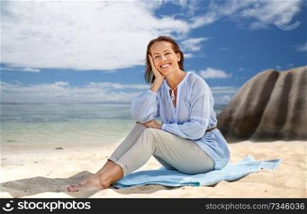 people and summer concept - happy smiling woman sitting on towel over seychelles island tropical beach background. happy woman over seychelles island tropical beach