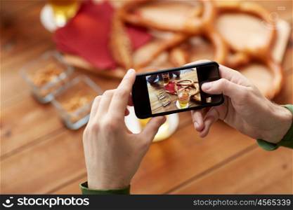 people and technology concept - close up of hands with smartphone picturing beer and pretzel at bar or pub. close up of hands with smartphone picturing beer