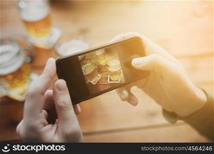 people and technology concept - close up of hands with smartphone picturing beer at bar. close up of hands with smartphone picturing beer