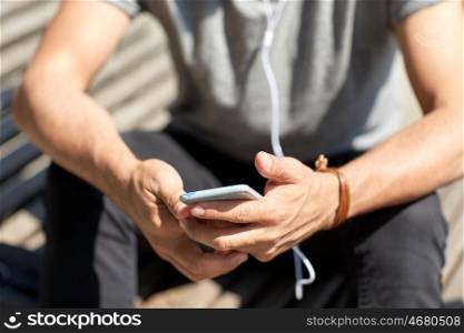 people and technology concept - close up of man with earphones and smartphone listening to music at brick wall on street. close up of man with smartphone and earphones wire
