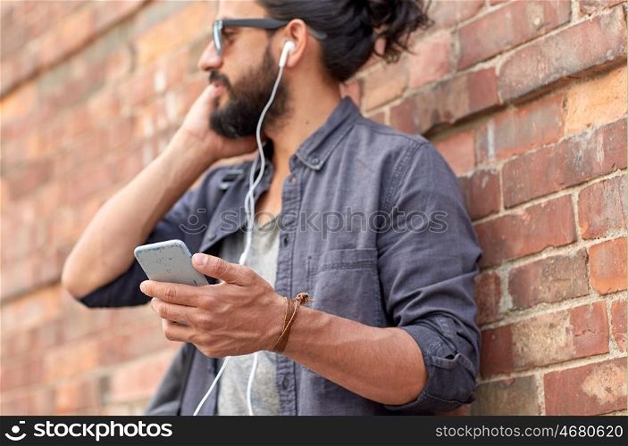people and technology concept - close up of man with earphones and smartphone listening to music at brick wall on street. man with earphones and smartphone on street