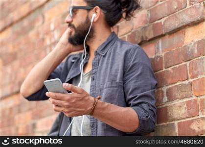 people and technology concept - close up of man with earphones and smartphone listening to music at brick wall on street. man with earphones and smartphone on street