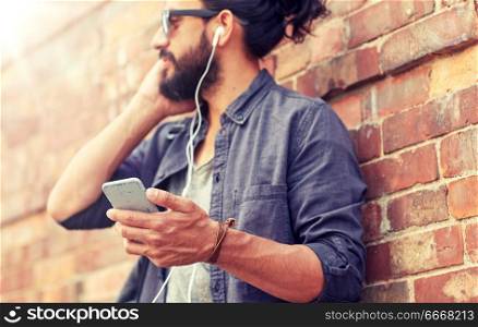 people and technology concept - close up of man with earphones and smartphone listening to music at brick wall on street. man with earphones and smartphone on street. man with earphones and smartphone on street