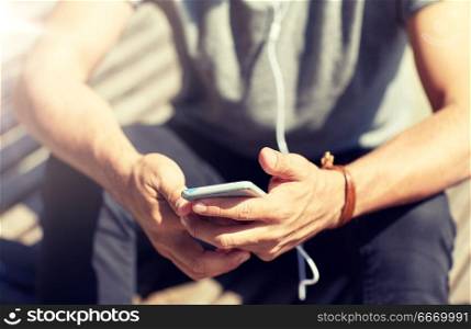 people and technology concept - close up of man with earphones and smartphone listening to music at brick wall on street. close up of man with smartphone and earphones wire. close up of man with smartphone and earphones wire