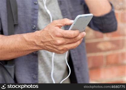 people and technology concept - close up of man with smartphone and earphones wire listening to music at brick wall on street. close up of man with smartphone and earphones wire