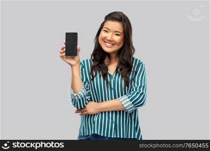 people and technology concept - happy asian young woman with smartphone over grey background. happy asian woman over grey background
