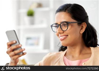 people and technology concept - happy indian woman using smartphone at home. happy indian woman using smartphone at home