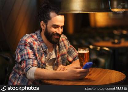 people and technology concept - happy man with smartphone drinking beer and reading message at bar or pub. man with smartphone and beer texting at bar