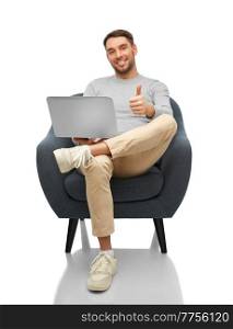 people and technology concept - happy smiling man with laptop computer sitting in chair and showing thumbs up gesture over white background. man with laptop sitting in chair showing thumbs up