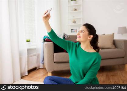people and technology concept - happy young woman taking selfie on smartphone at home. happy young woman taking selfie with smartphone