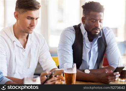 people and technology concept - male friends with smartphone drinking beer at bar or pub. male friends with smartphone drinking beer at bar