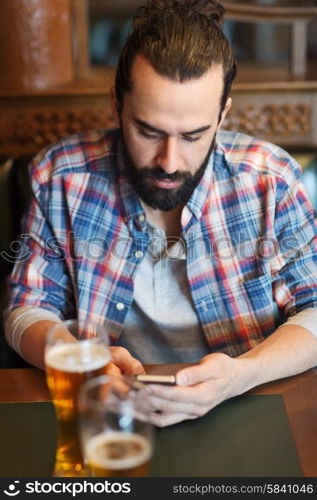 people and technology concept - man with smartphone drinking beer and reading message at bar. man with smartphone drinking beer at bar