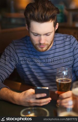 people and technology concept - man with smartphone drinking beer and reading message at bar. man with smartphone drinking beer at bar