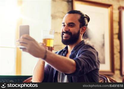 people and technology concept - man with smartphone drinking beer and taking selfie at bar or pub. man with smartphone drinking beer at bar or pub. man with smartphone drinking beer at bar or pub