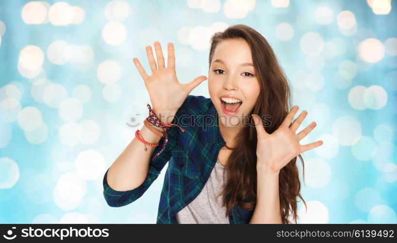 people and teens concept - happy laughing pretty teenage girl showing hands over blue holidays lights background. happy laughing pretty teenage girl showing hands