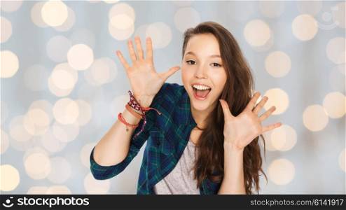 people and teens concept - happy laughing pretty teenage girl showing hands over holidays lights background. happy laughing pretty teenage girl showing hands