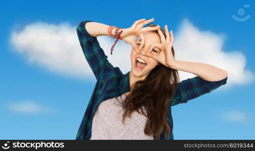 people and teens concept - happy smiling pretty teenage girl making face and having fun over blue sky and clouds background. happy teenage girl making face and having fun