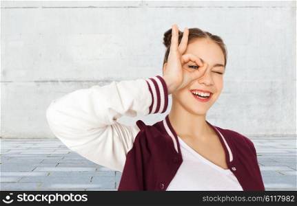 people and teens concept - happy smiling pretty teenage girl making face and having fun over gray urban street background. happy teenage girl making face and having fun
