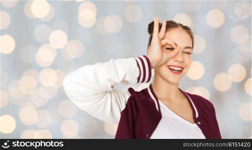 people and teens concept - happy smiling pretty teenage girl making face and having fun over holidays lights background. happy teenage girl making face and having fun