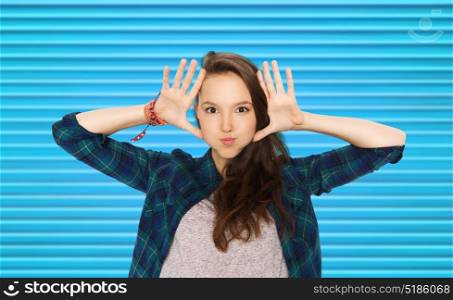 people and teens concept - happy smiling pretty teenage girl making faces and having fun over blue ribbed background. happy teenage girl making face and having fun
