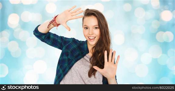 people and teens concept - happy smiling pretty teenage girl showing hands over blue holidays lights background. happy smiling pretty teenage girl showing hands