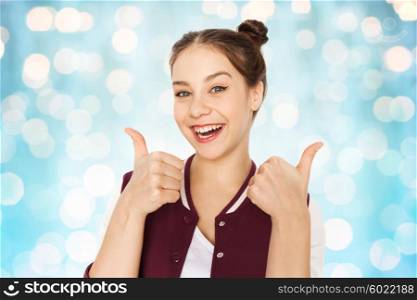 people and teens concept - happy smiling pretty teenage girl showing thumbs up over blue holidays lights background. happy smiling teenage girl showing thumbs up