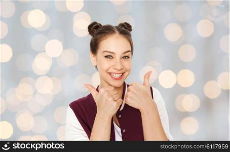 people and teens concept - happy smiling pretty teenage girl showing thumbs up over holidays lights background. happy smiling teenage girl showing thumbs up