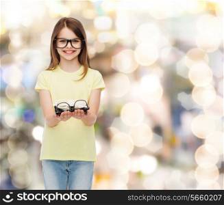 people and vision concept - smiling cute little girl in black eyeglasses holding many glasses in her hands