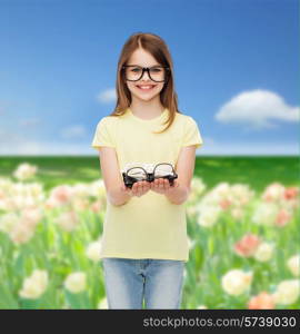 people and vision concept - smiling cute little girl in black eyeglasses holding many glasses in her hands