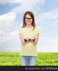 people and vision concept - smiling cute little girl in black eyeglasses holding many glasses in her hands