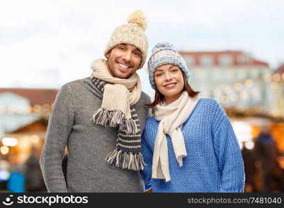 people and winter holidays concept - happy couple in knitted hats and scarves over christmas market in old town of tallinn city background. happy couple in winter clothes at christmas market