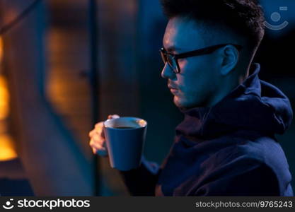 people and work concept - close up of young man in glasses drinking coffee in dark room. young man in glasses drinking coffee in dark room