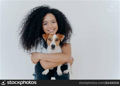 People, animal or pet care concept. Curly haired woman embraces favourite dog, smiles pleasantly, stands against white background, copy space area for your advertising content. Good friends.